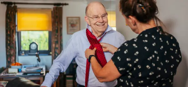 A carer helps to put on elderly man's tie