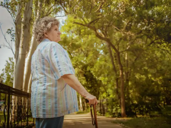 An elderly woman holding a cane while standing straight