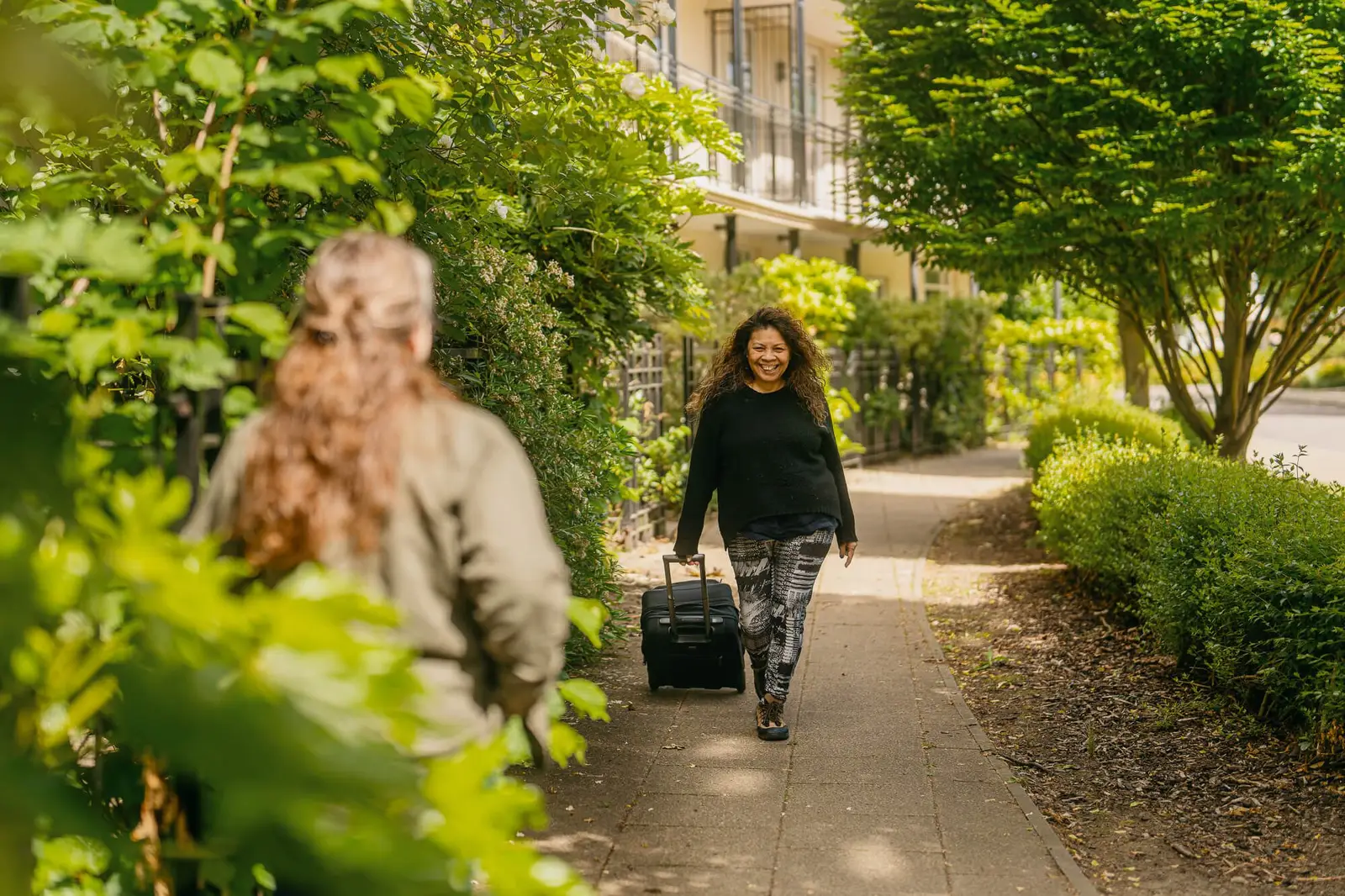 An Elder Live-In Carer arrives at her clients home and is met by the clients daughter at the front garden.