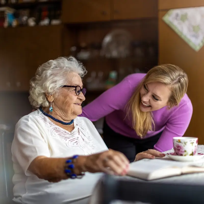 Elderly woman sitting with a book and cup of tea with her carer