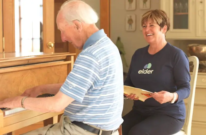 Elderly man plays piano whilst his carer watches