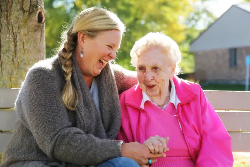 Carer with elderly woman sitting on a bench and smiling