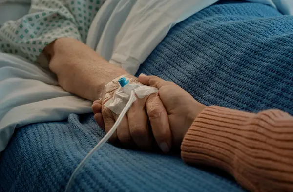 Elderly person holding loved one's hand in hospital