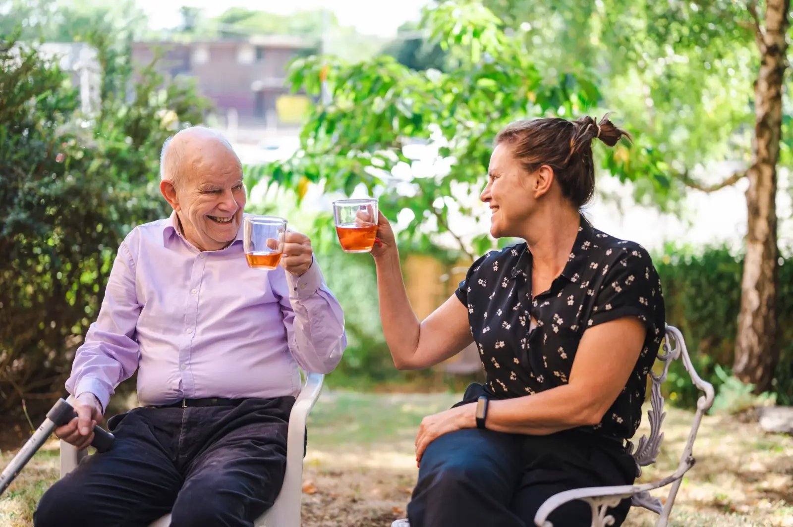 Old man with carer outdoors enjoying a hot drink