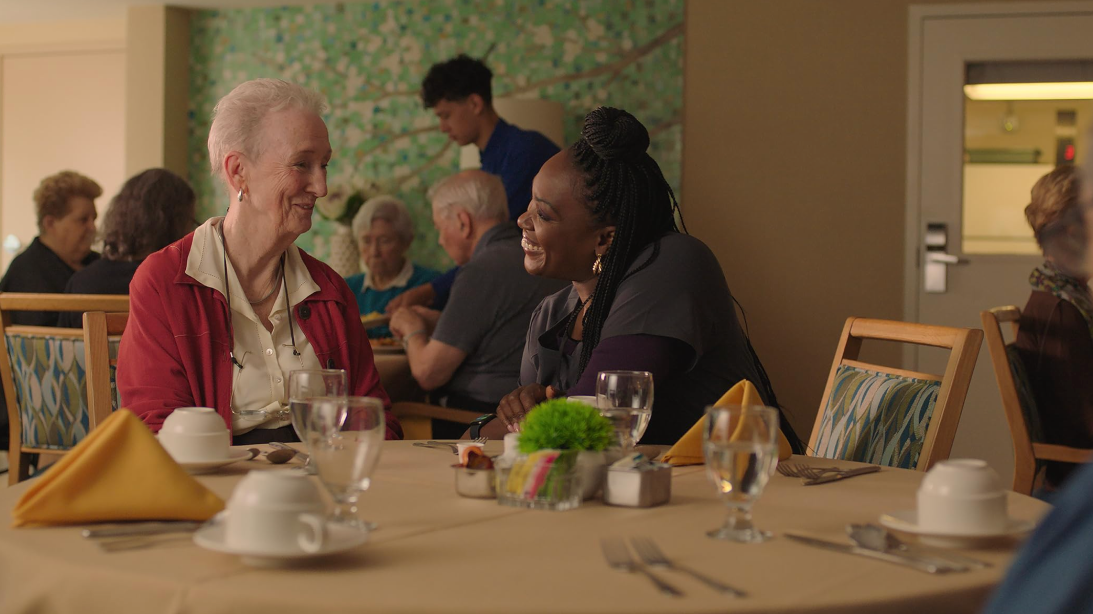 Ruth, an older woman living with dementia, shares a warm moment with her care worker over lunch in Familiar Touch (2024)