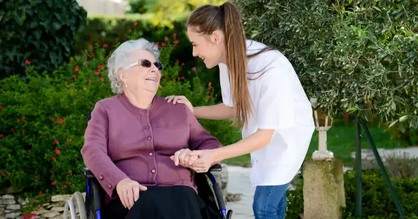 Elderly woman in a wheelchair speaking with her carer in the garden