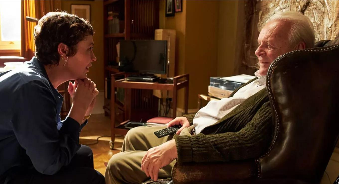 A daughter kneels to talk gently with her father, who is living with dementia, in The Father (2020)