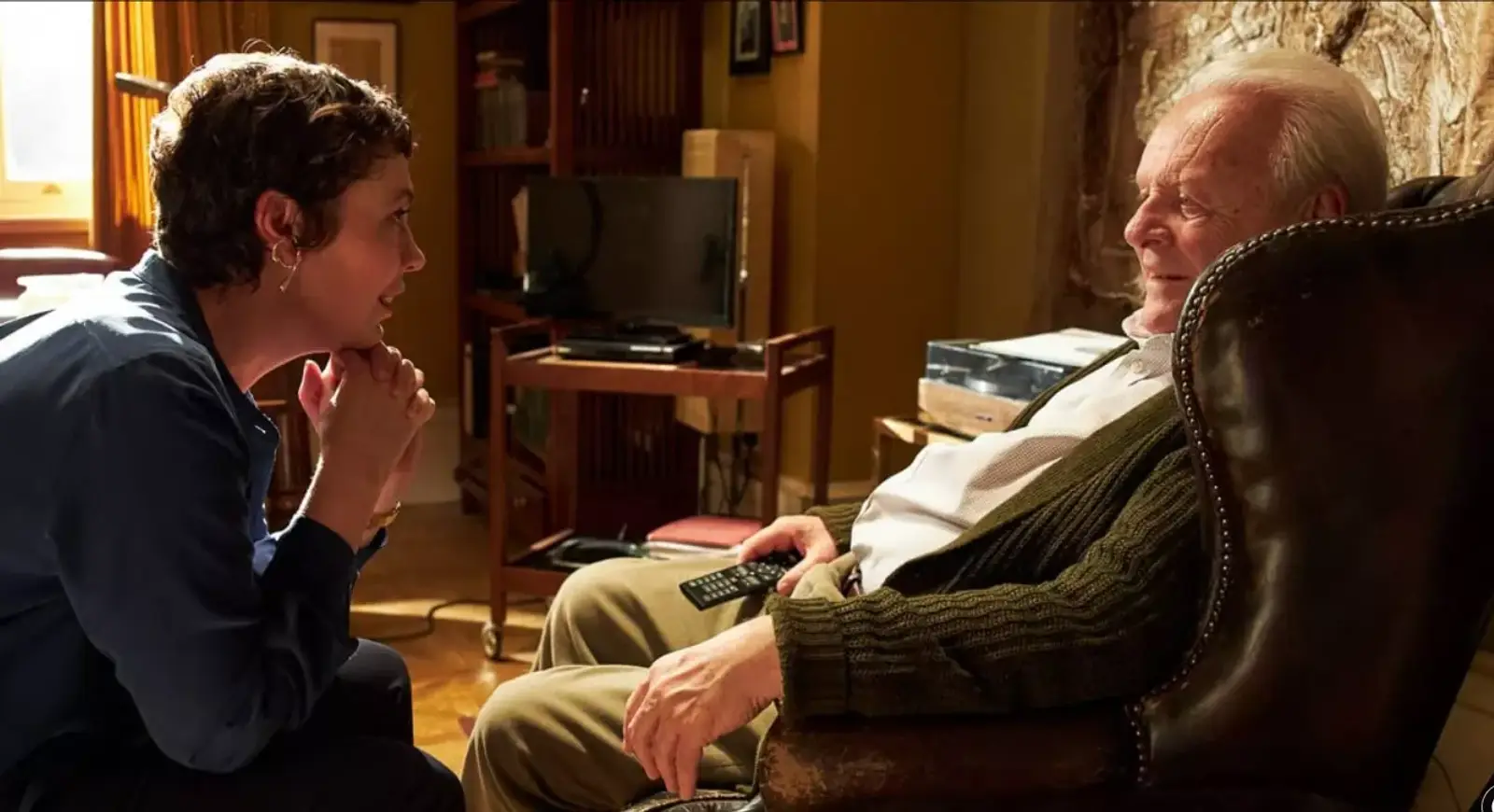 A daughter kneels to talk gently with her father, who is living with dementia, in The Father (2020)