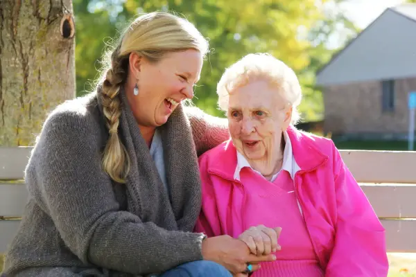 Elderly woman laughing on a bench with carer