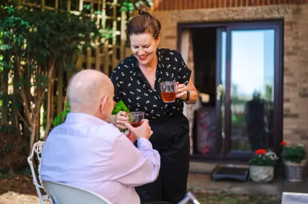 Carer in the garden giving tea to elderly man