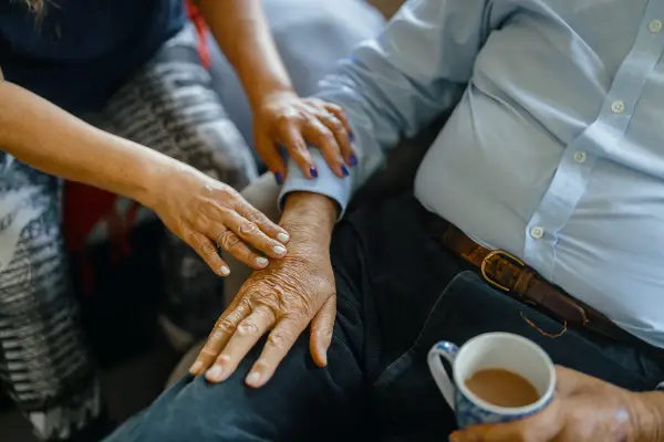 An person holding the hand of an elderly man who's drinking tea