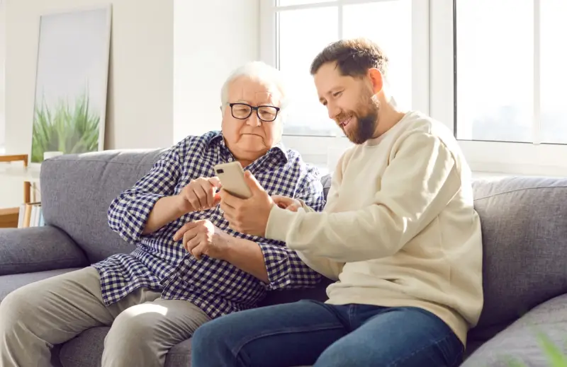 Elderly man looking at phone with his carer