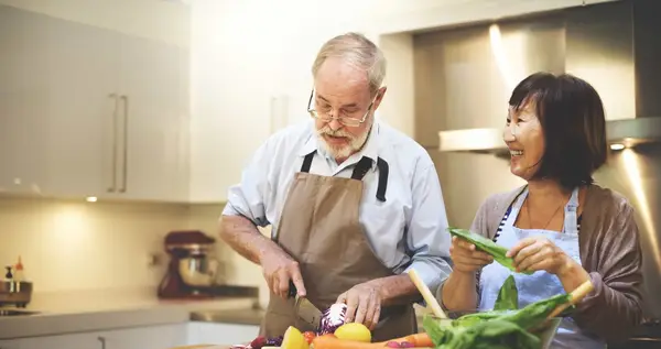Elderly man chopping vegetables with carer
