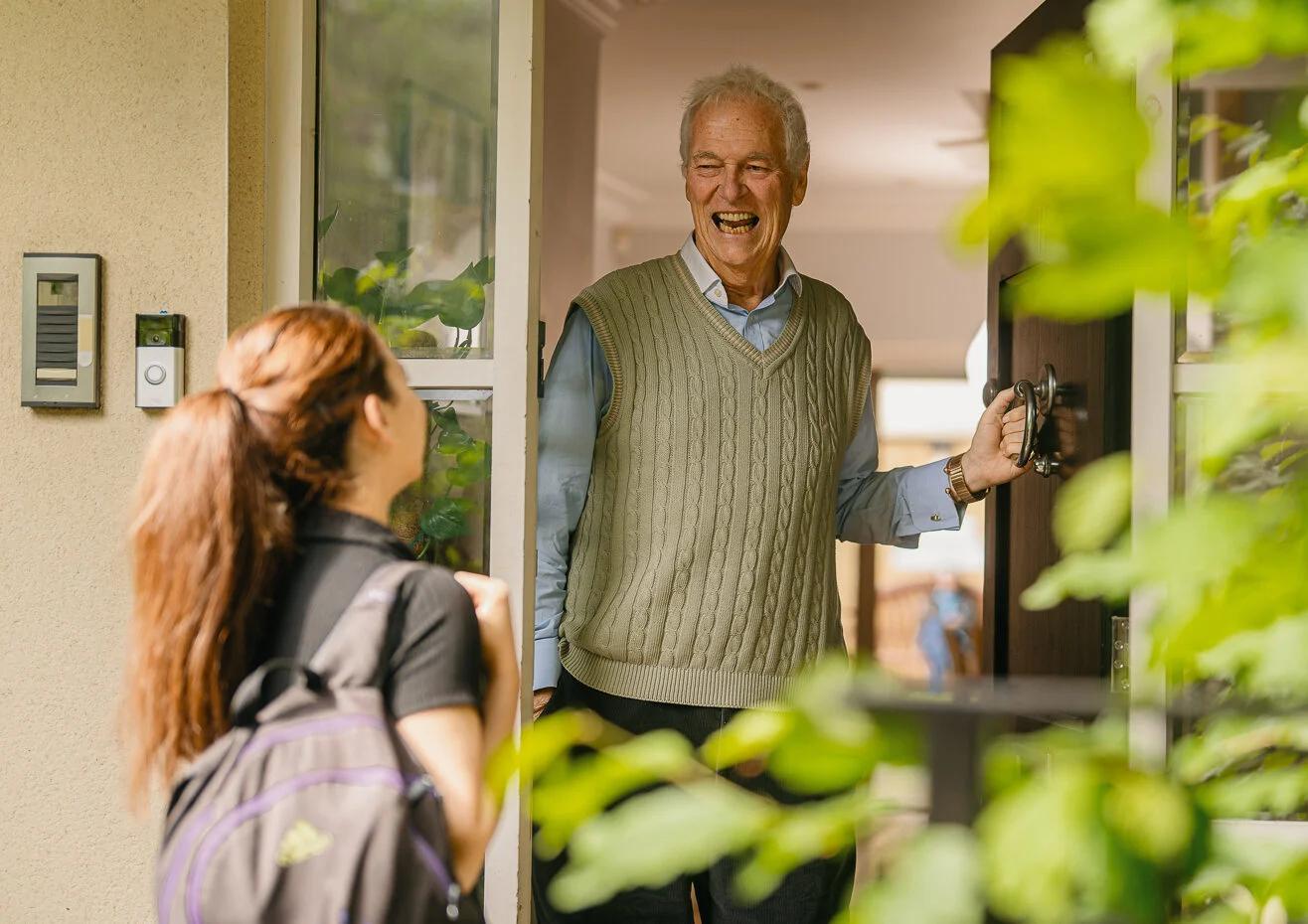 Elderly man opening the door for a carer