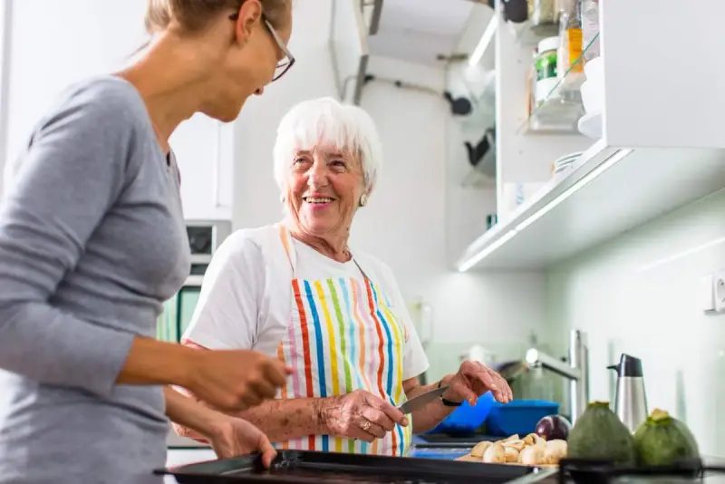Elderly woman and carer cook together