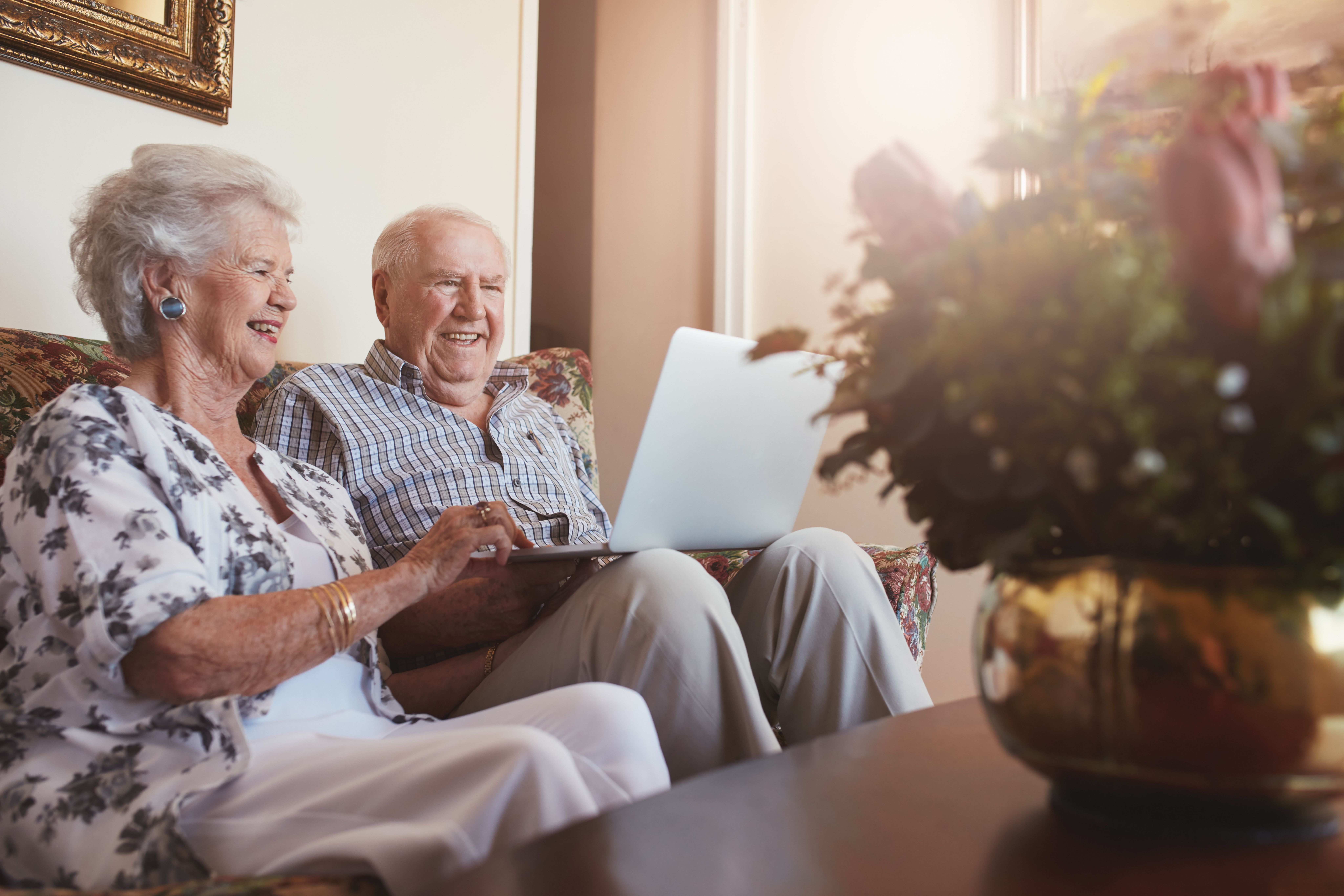 An elderly couple smiling while looking at their laptop