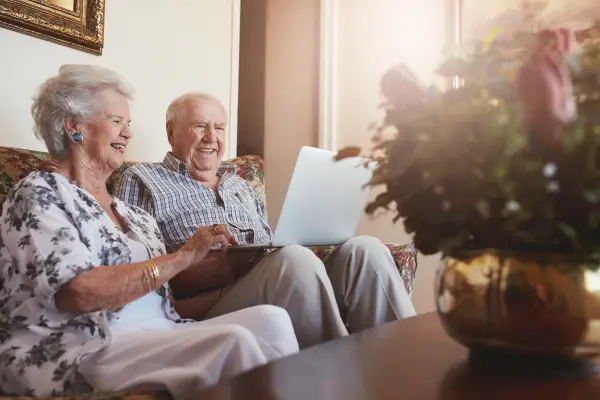 An elderly couple smiling while looking at their laptop