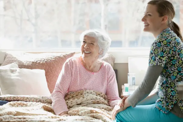 Older woman in bed with her carer sitting next to her