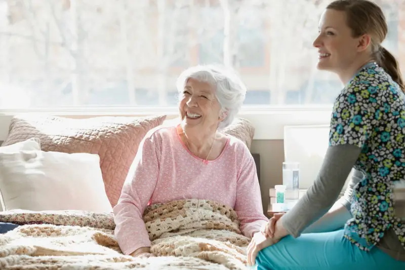 Carer sitting next to elderly woman in bed