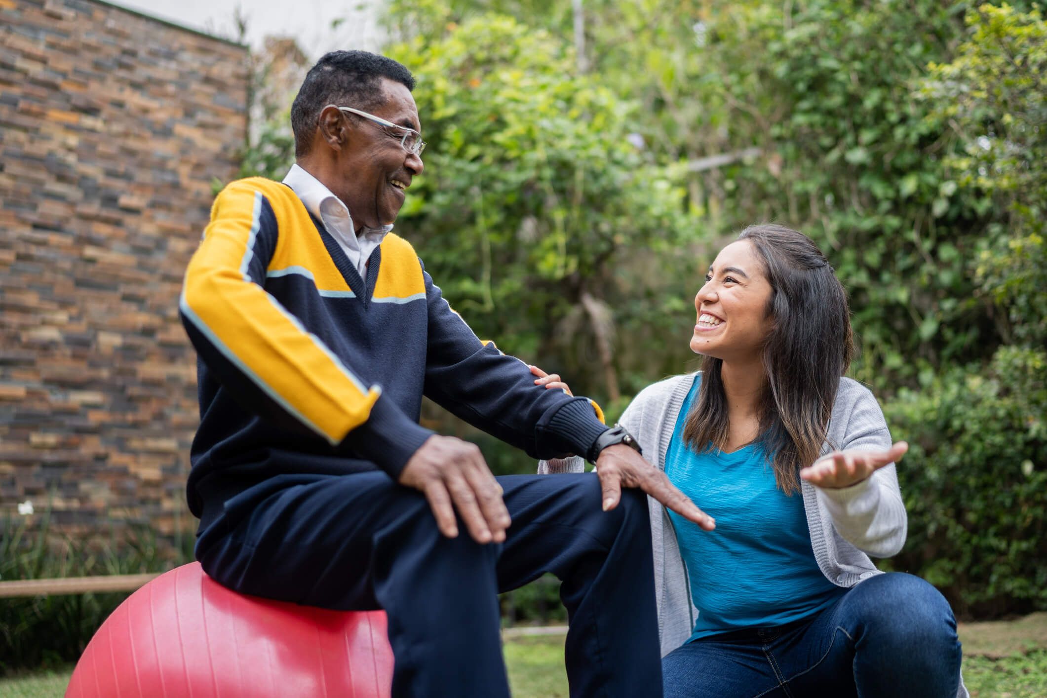 Elderly man talking to a carer while sitting on an exercise ball