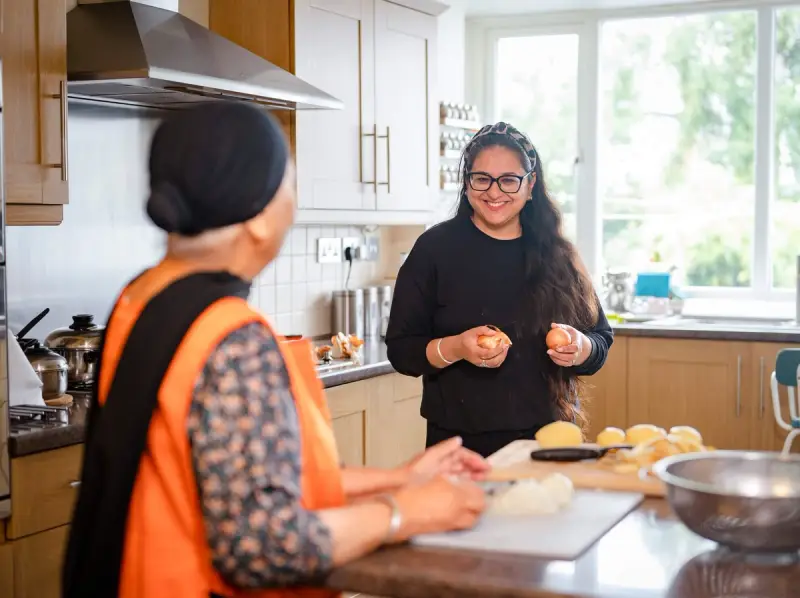 Carer and elderly woman cooking and laughing in the kitchen