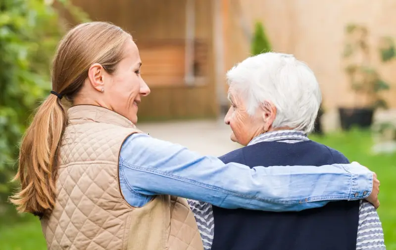 Carer holding the shoulders of an elderly woman and smiling