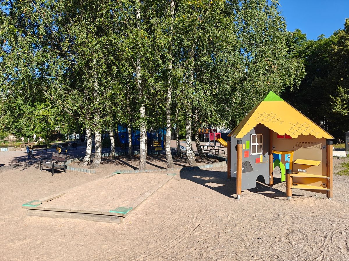 Hiekkalaatikko ja pieniä mökkimäisiä leikkielementtejä.