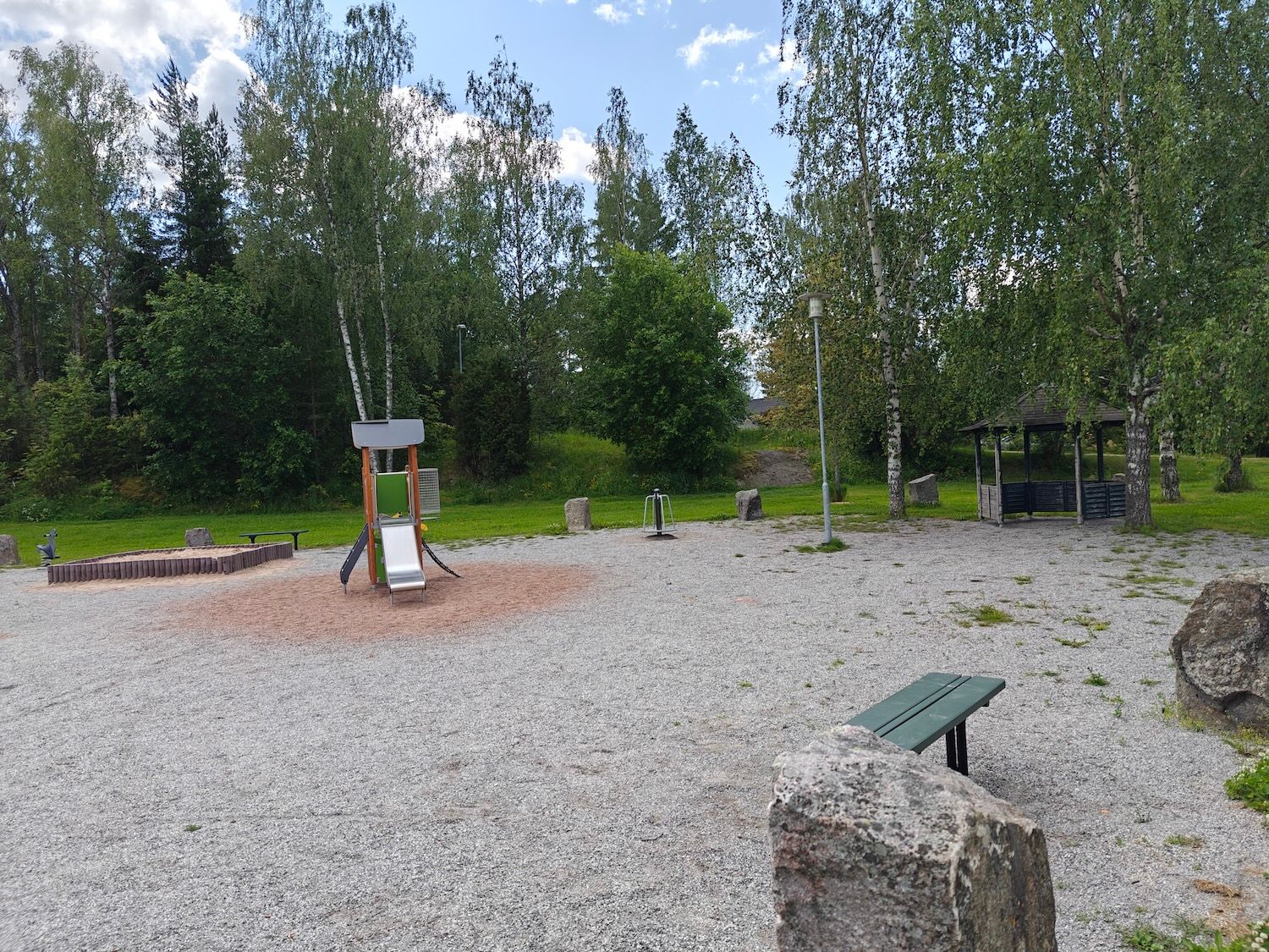 Hiekkalaatikko, pieni liukumäki, karuselli, penkki ja katos.