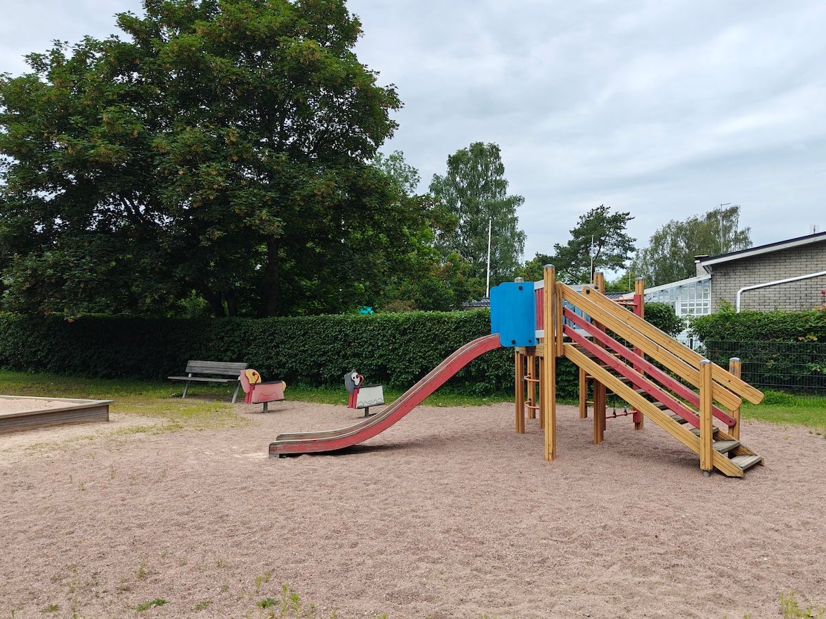 Liukumäki, kaksi jousivälinettä ja hiekkalaatikon kulma.