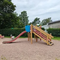 Liukumäki, kaksi jousivälinettä ja hiekkalaatikon kulma.