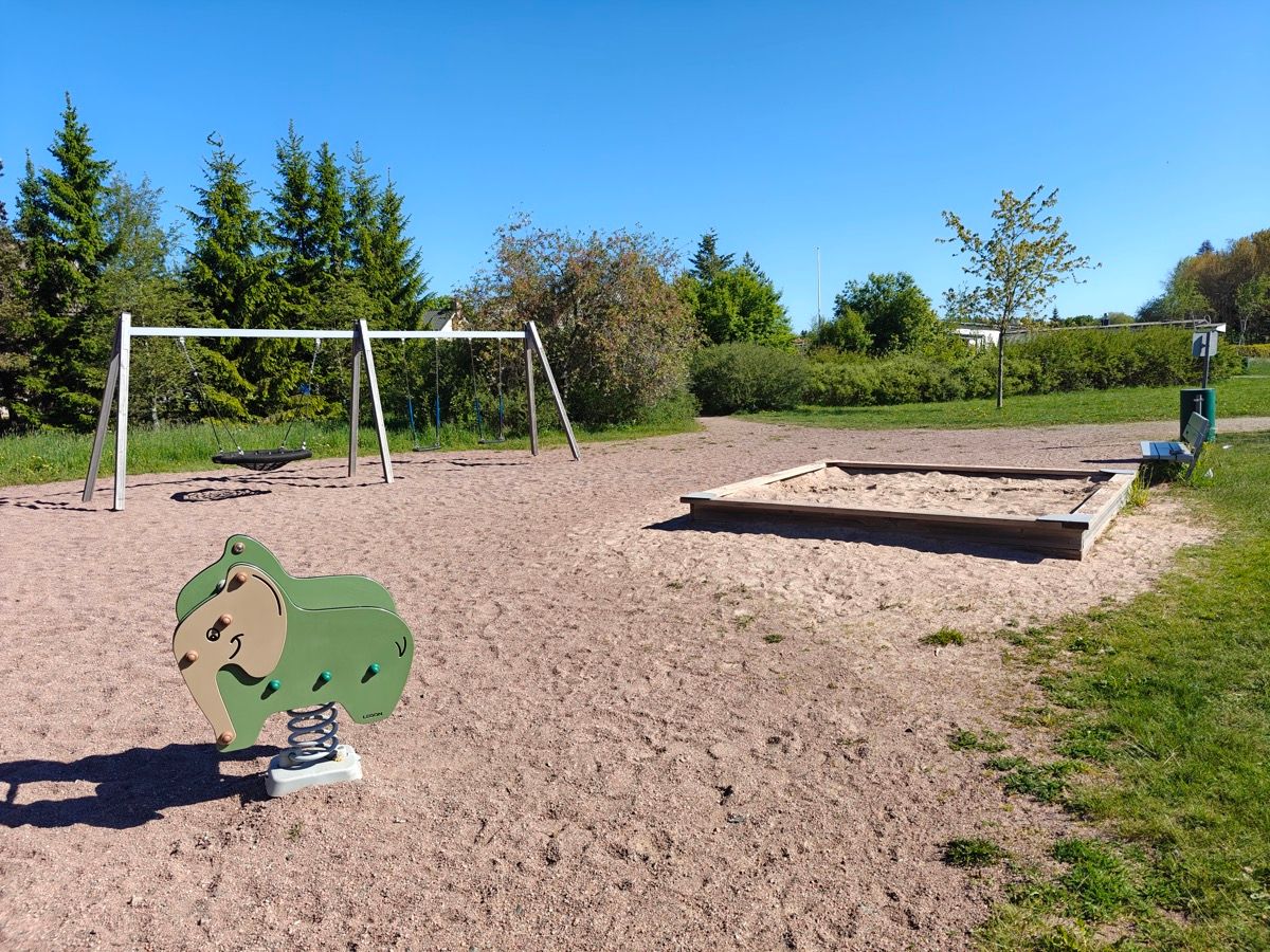 Hiekkalaatikko ja jousiväline, taustalla keinut.