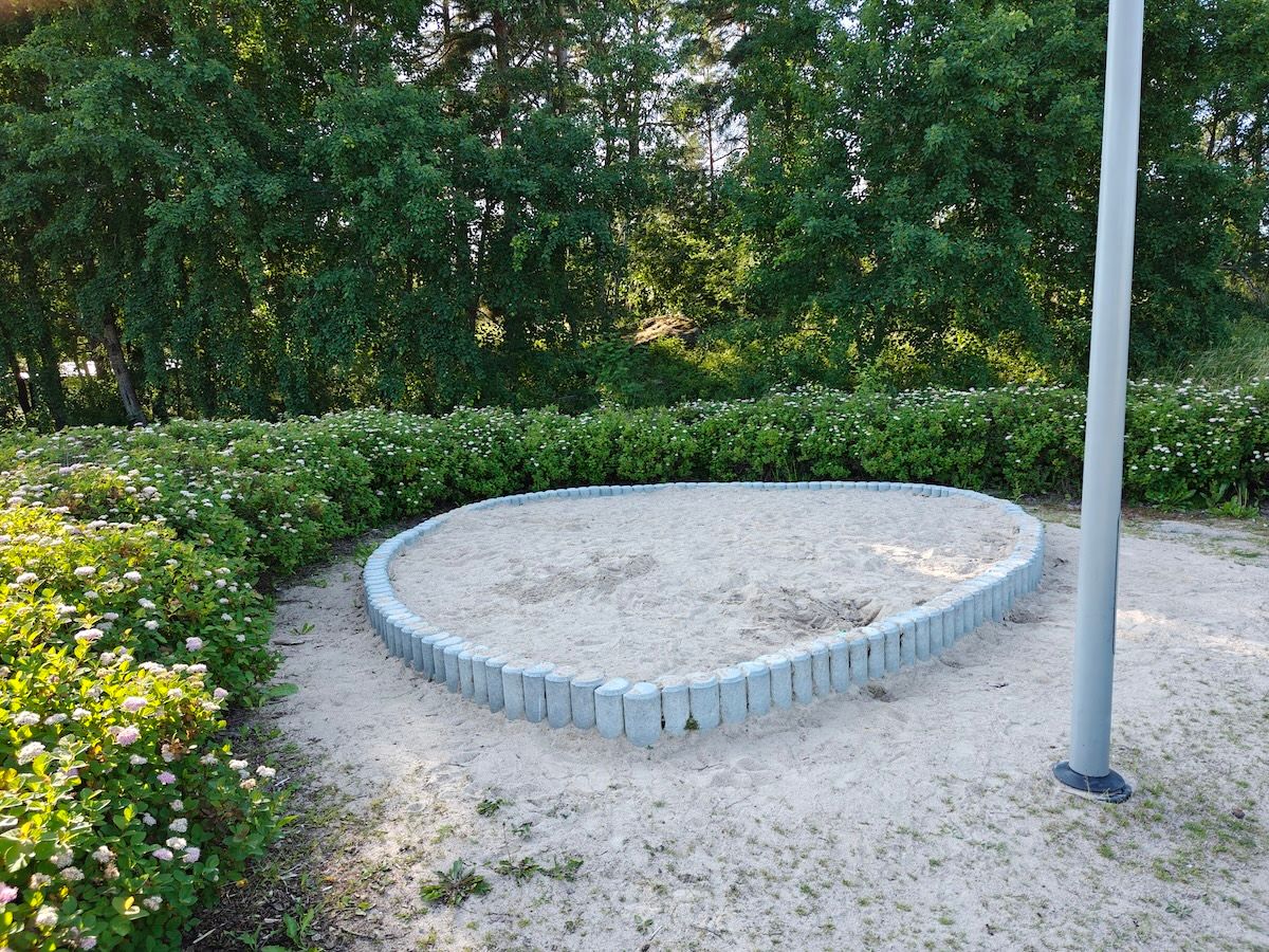 Kukkapuskien ympäröimä hiekkalaatikko.
