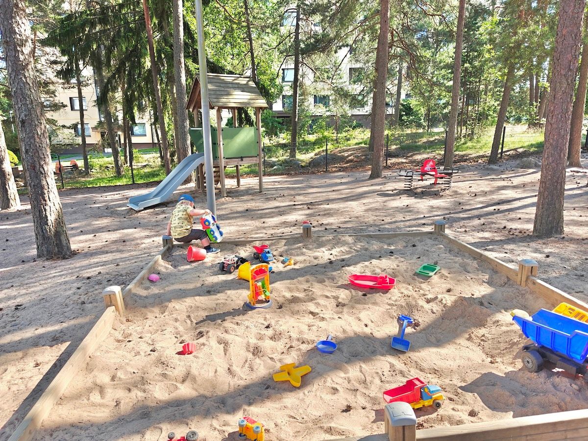 Hiekkalaatikko, liukumäki ja jousiväline.