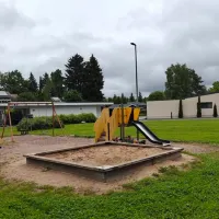 Etualalla hiekkalaatikko. Taustalla vauvakeinu, lautakeinu sekä liukumäki. Hiekkalaatikon vieressä kaksi jousivälinettä.