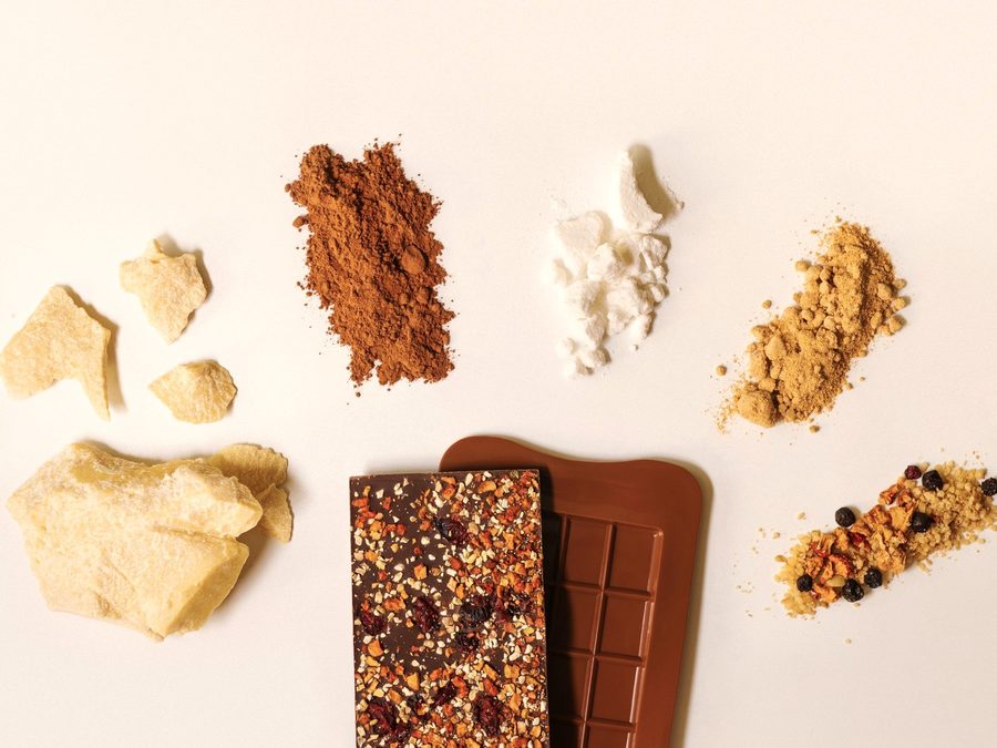 Bar ingredients laid out for formulation: cocoa, protein powder, nuts and a chocolate slab