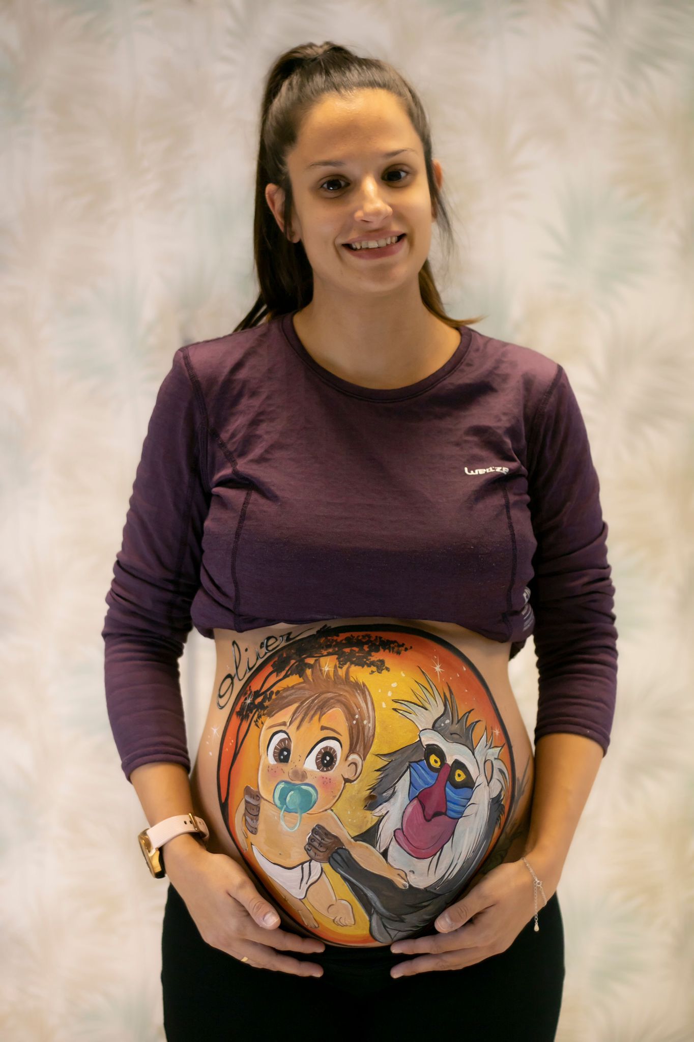 Mujer embarazada posando con diseño de bellypainting de rafiki elevando a un bebé 