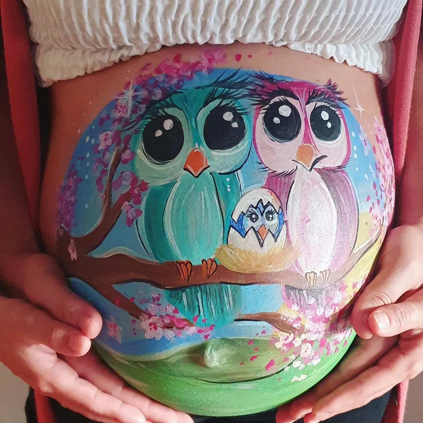 Diseño de bellypainting  en la barriga de una mujer embarazada en el que aparecen dos búhos con su pollito saliendo del cascarón en un cerezo y durante un amanecer