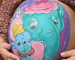 Mujer embarazada posando con diseño de bellypainting de dumbo y su mama