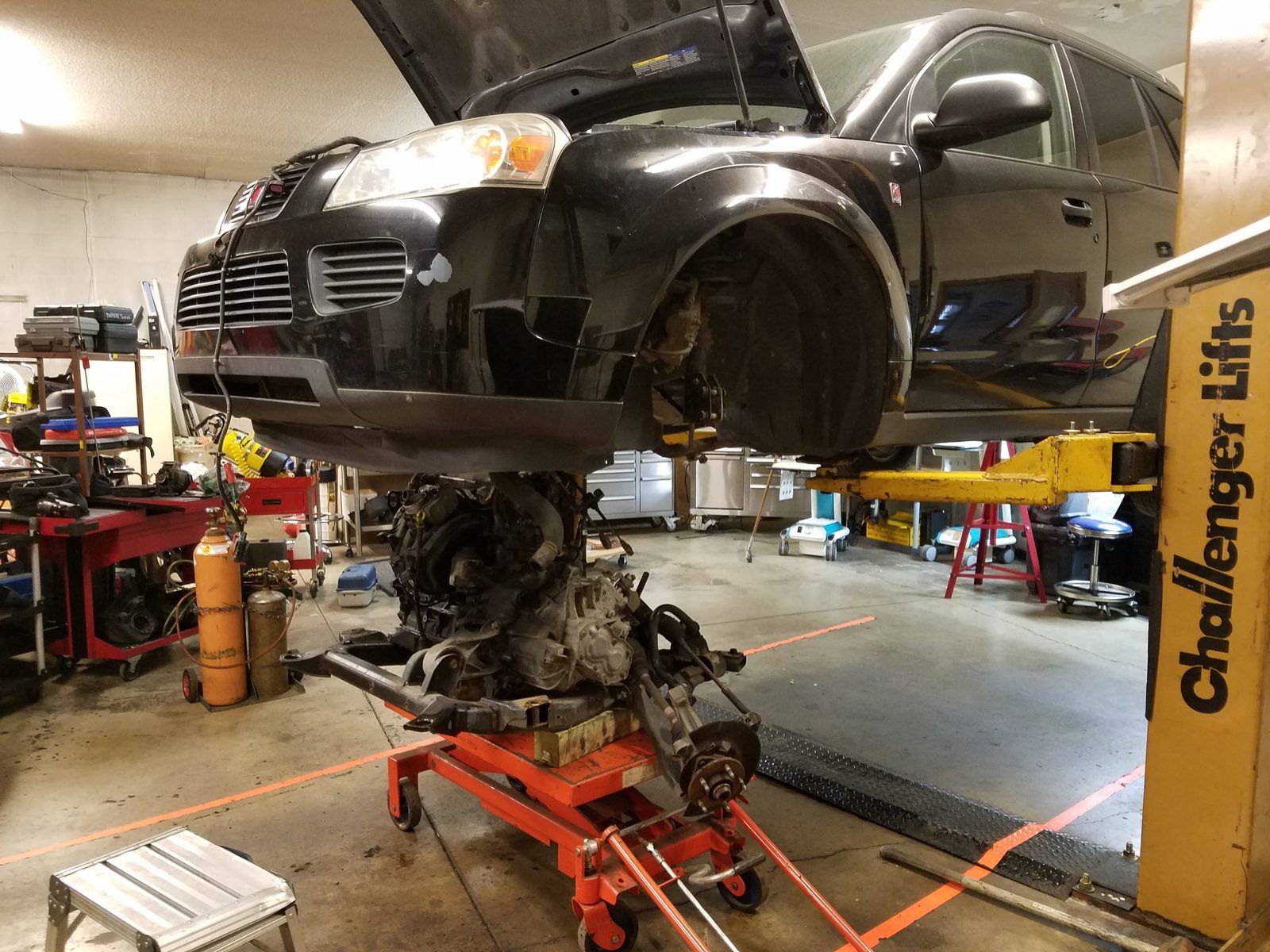 Front-wheel-drive engine and transaxle cradle lowered out of an SUV on a transmission jack at Speedy Underhood Service in Columbus, Ohio