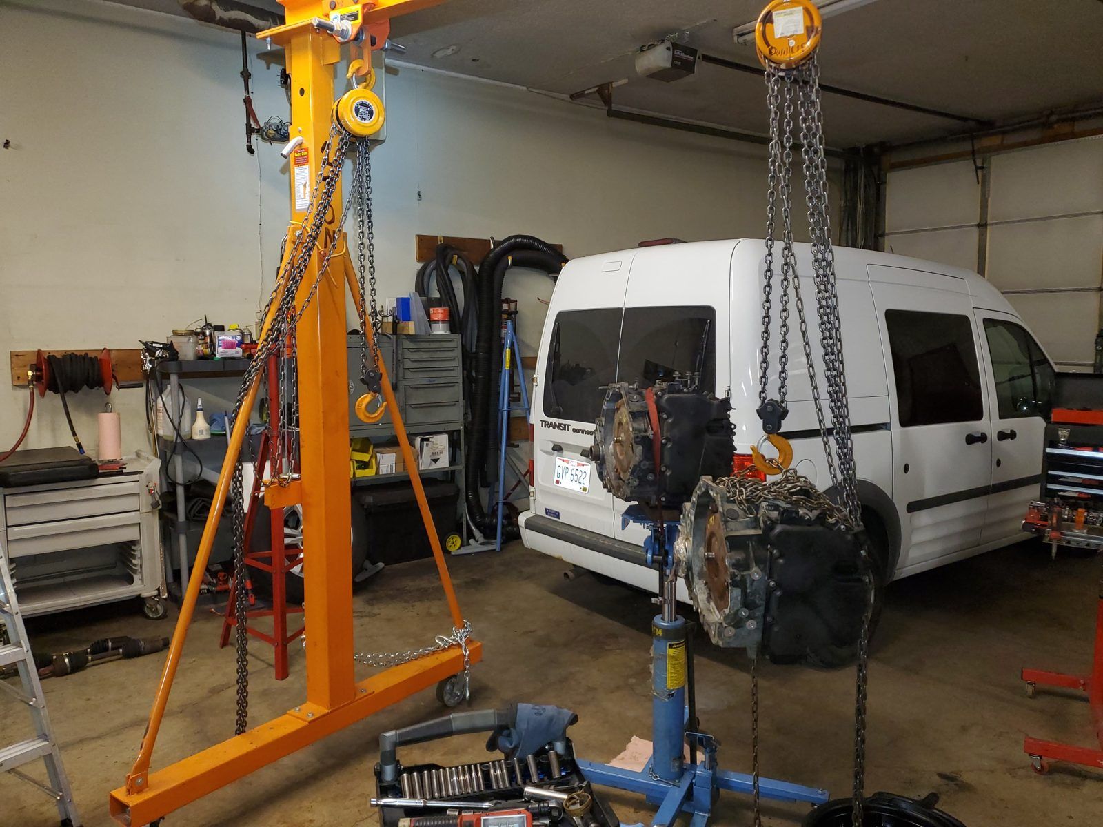 Transmission suspended from a gantry hoist beside a Ford Transit Connect van at Speedy Underhood Service in Columbus, Ohio