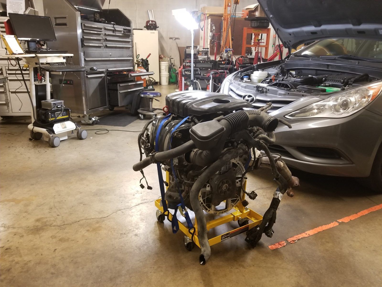 Complete engine assembly on a lift table in front of the sedan it came out of at Speedy Underhood Service in Columbus, Ohio