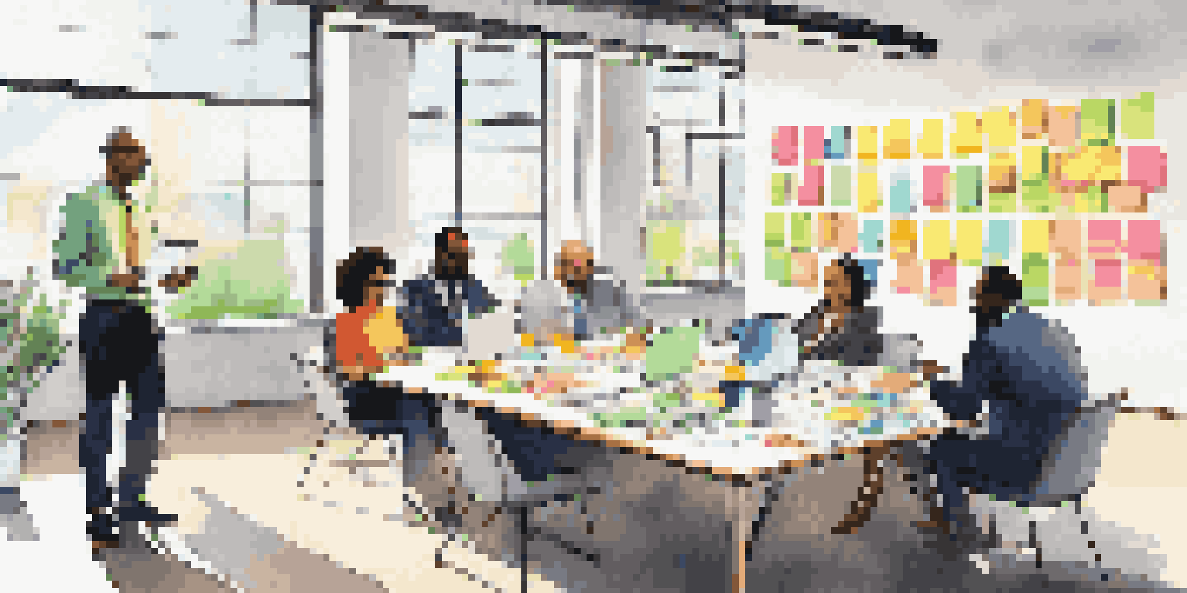 A diverse group of business leaders collaborating around a table with sticky notes and laptops in a bright office.