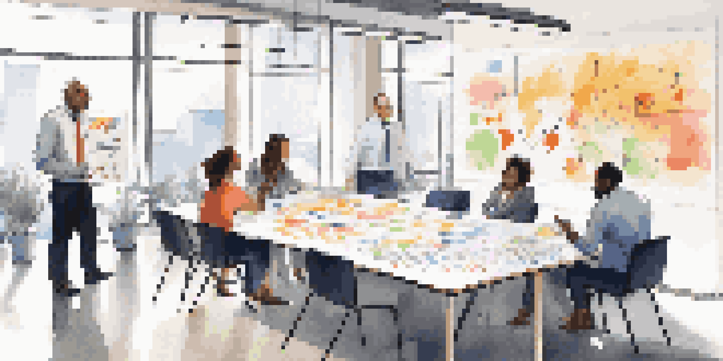 A diverse group of colleagues discussing ideas around a table in a bright office, with a whiteboard covered in notes and diagrams.