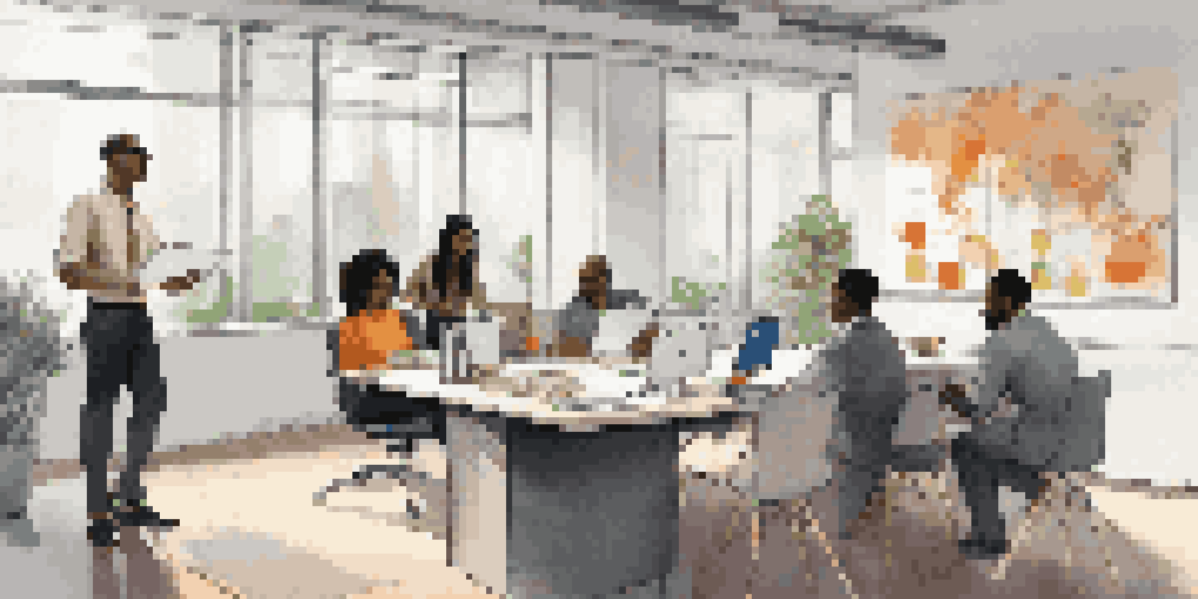 A diverse group of employees in a bright modern office discussing around a conference table.