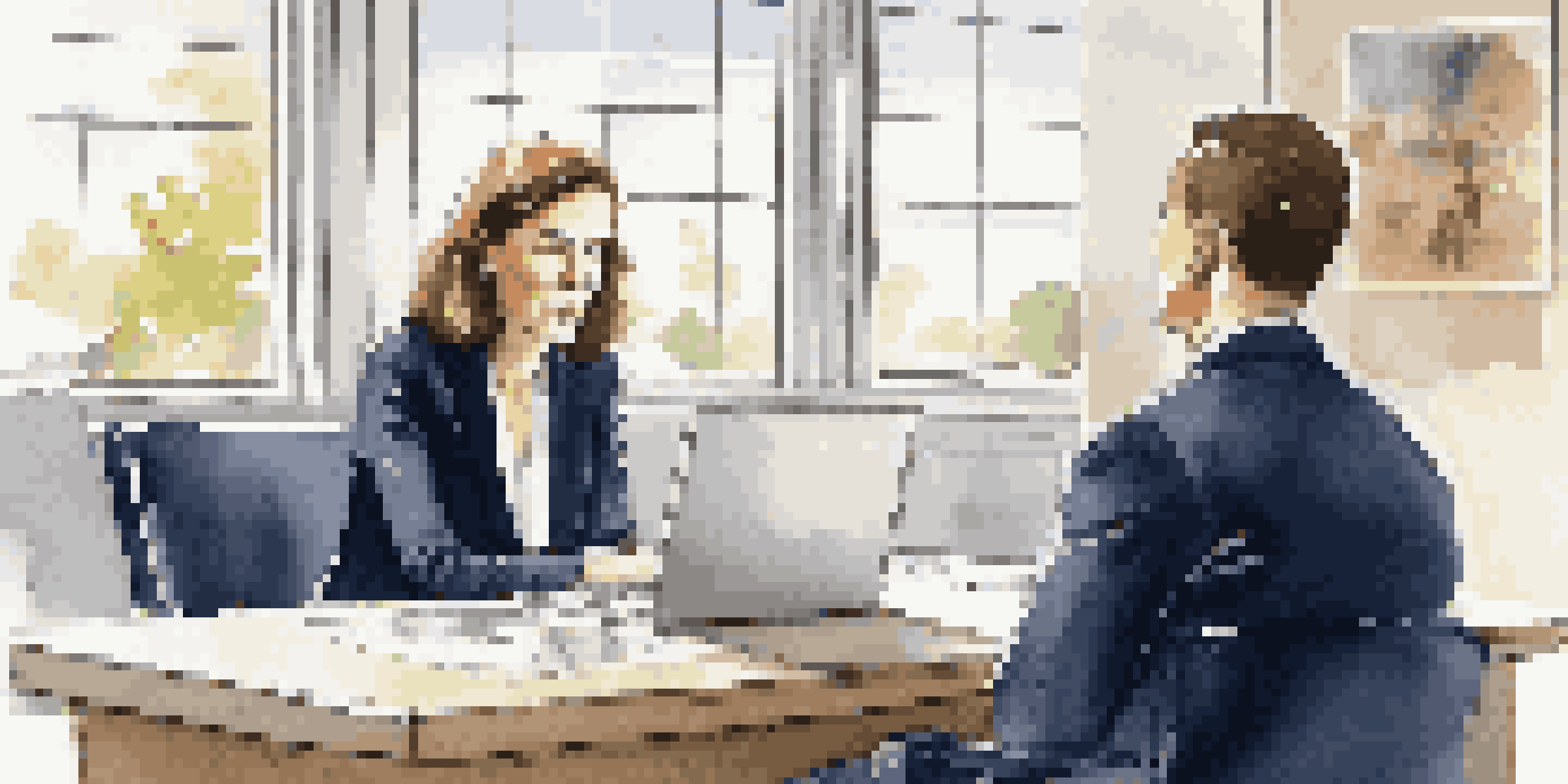 A career coach and client sitting in a bright office, engaged in a discussion, with a laptop on the desk and motivational poster on the wall.