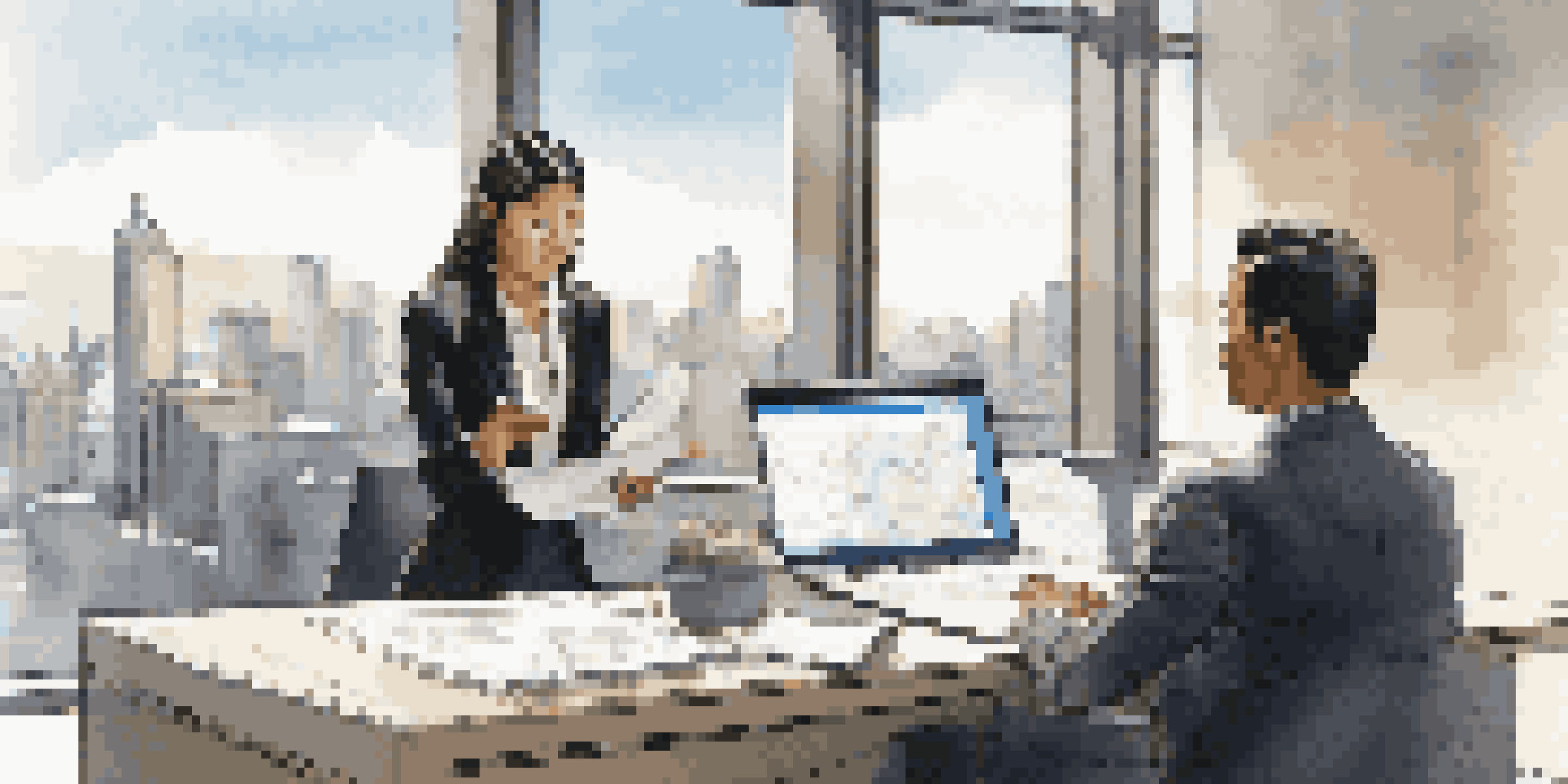 A young Asian woman in formal attire sitting at a modern desk, looking at salary data on a laptop with a city skyline in the background.