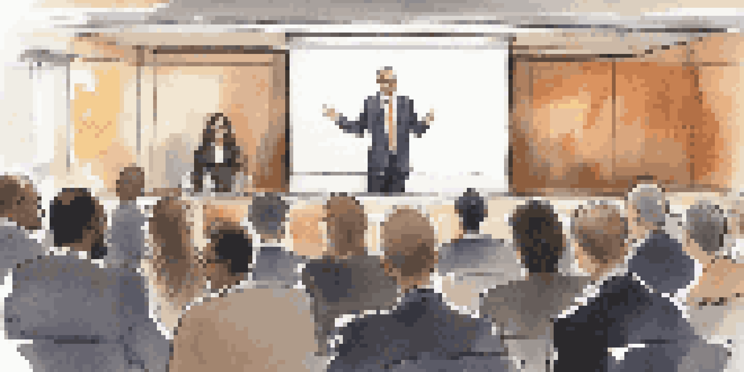A confident speaker at a podium engaging a diverse audience in a modern conference hall.