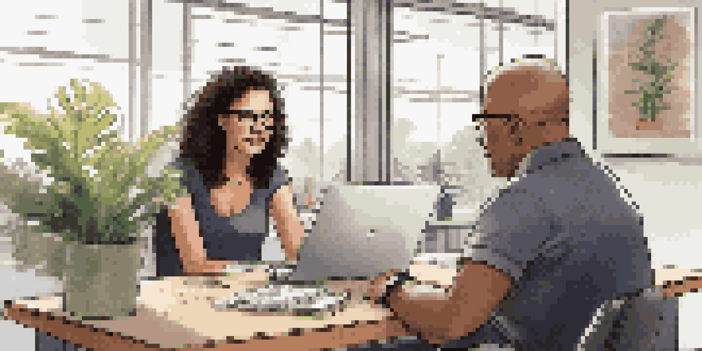A mentor showing a presentation on a laptop to a young mentee in a bright office, with plants and motivational posters around them.