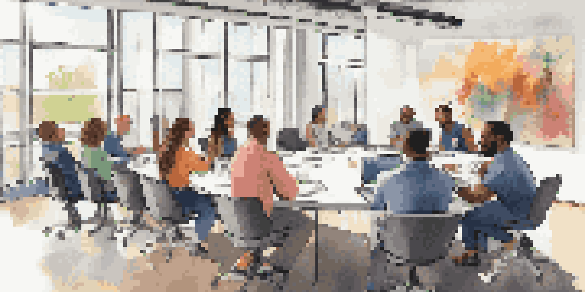 A diverse group of employees in a bright meeting room, collaborating around a conference table with laptops.