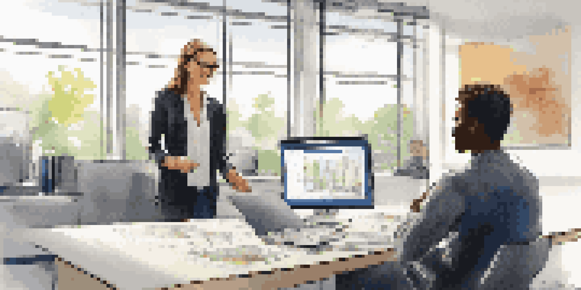 A mentor shows a young adult a project on a computer in a bright office, with both individuals engaged in the learning process.